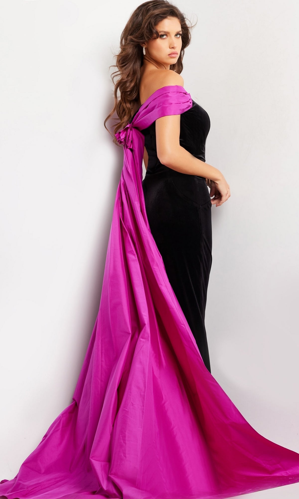 A woman poses in the Long Prom Dress 37375 by Jovani, featuring a black off-the-shoulder design with a dramatic bright pink satin train, set against a plain white background.